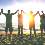 砂浜で太陽に向かって繋いだ手を上げる若者たち