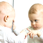 鏡に映った自分を指差す赤ちゃん